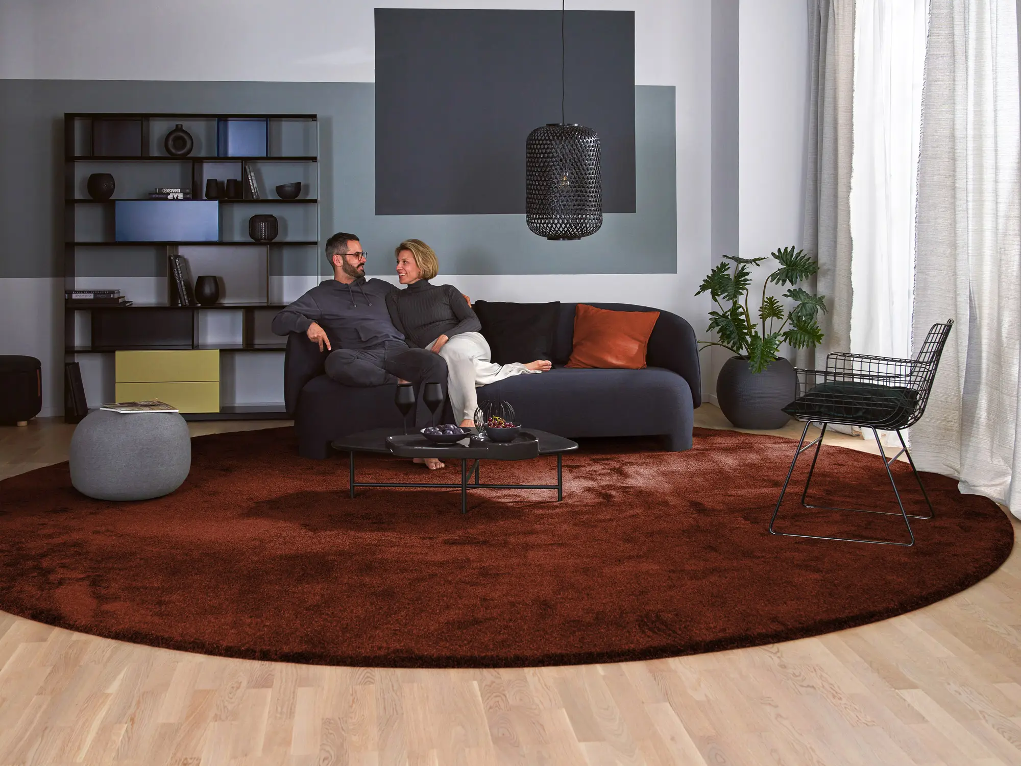 Runder Hochflorteppich Brienne von Ruxedo in Kupferrot im Wohnzimmer mit dunklem Sofa und modernen Deko-Elementen