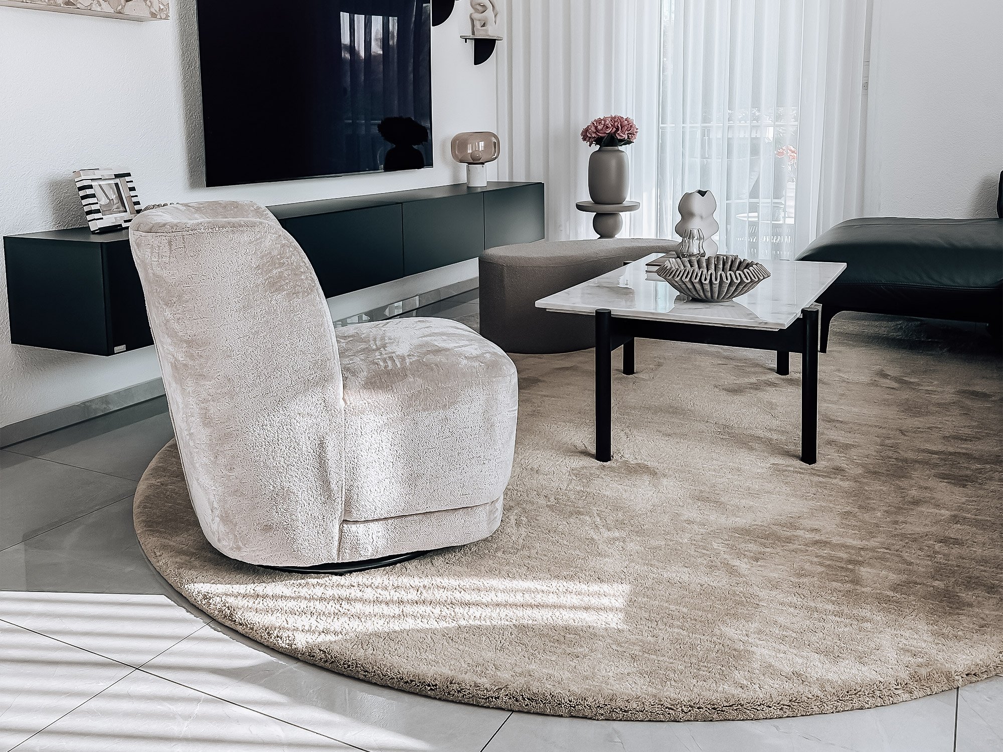 Runder Hochflorteppich „Hilda“ in Taupe von Ruxedo, dekorativ inszeniert im modernen Wohnzimmer mit Sessel, Couchtisch und TV-Möbel