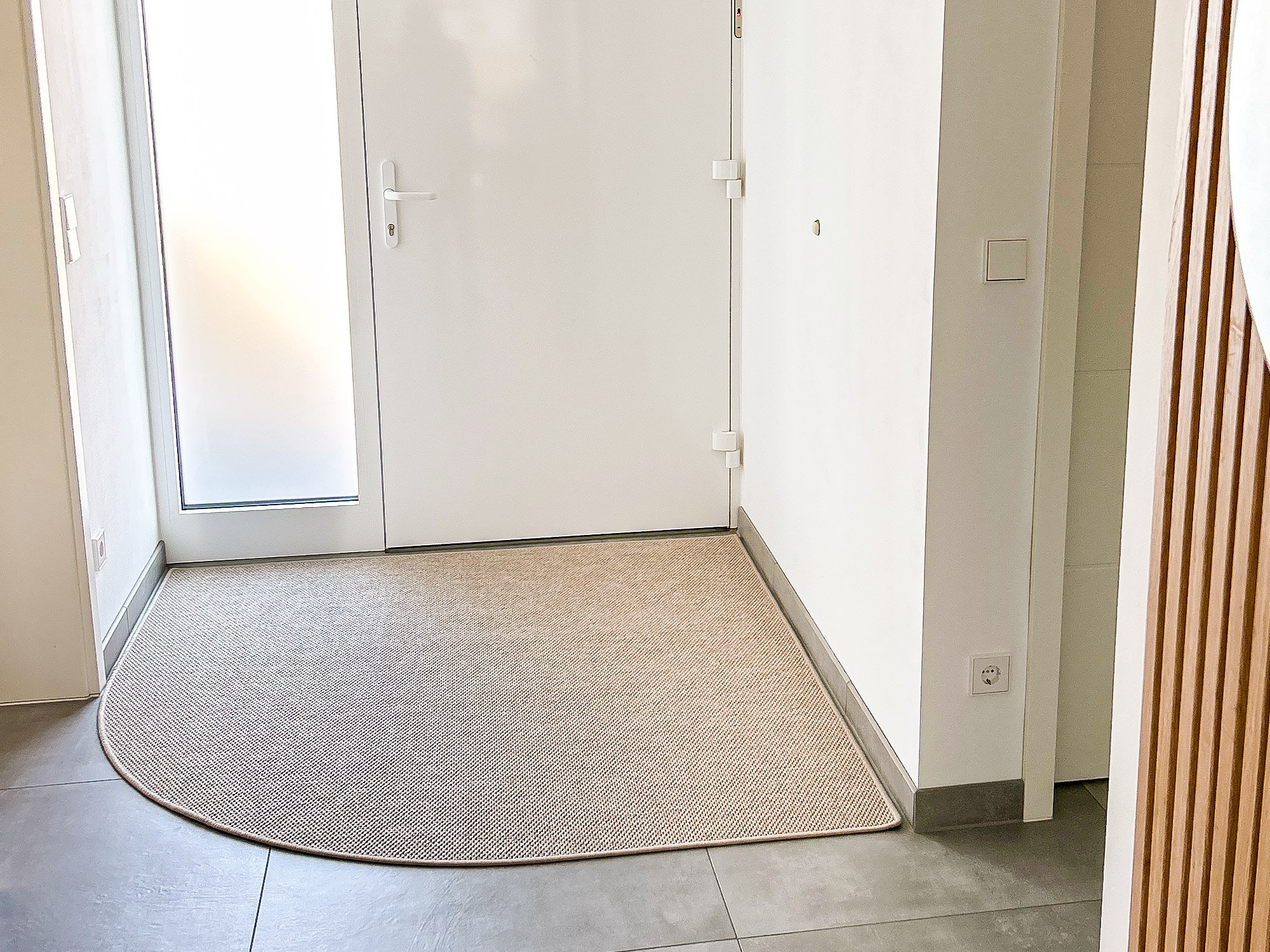 Die beige Fußmatte Mailo in der persönlichen Wuschform eines Kunden liegt vor einer Haustür im Innenbereich