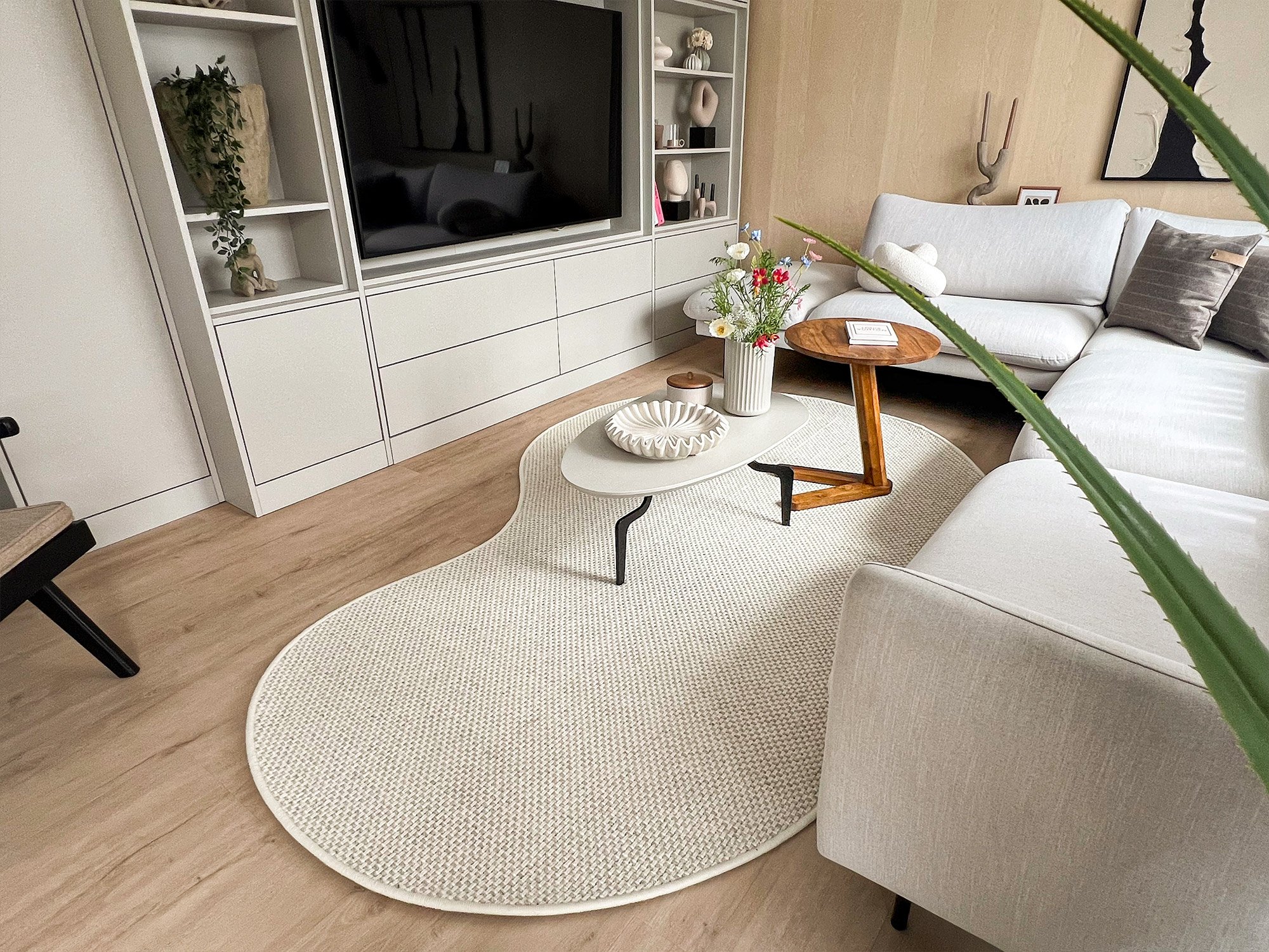 Der Oujda Wollteppich als organische Form Bean in Beige liegt in einem hell eingerichteten Wohnzimmer vor dem Sofa