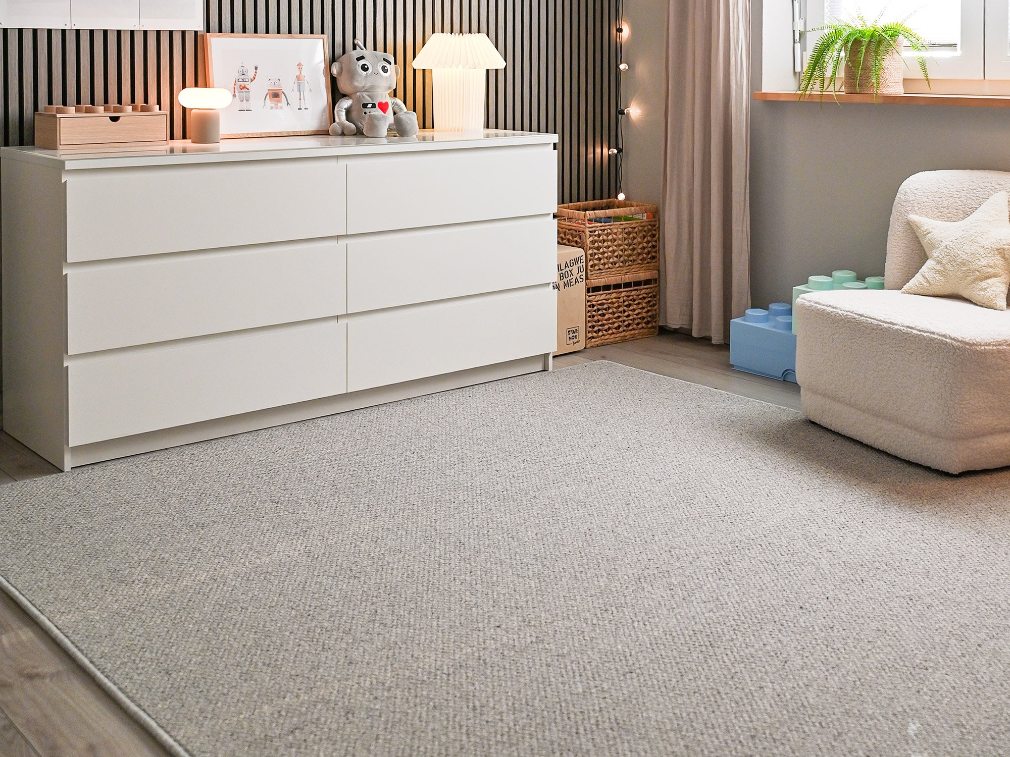 Rechteckiger Wollteppich Tetouan in Hellgrau in modernem Kinderzimmer mit weißer Kommode, Sessel und sanfter Beleuchtung