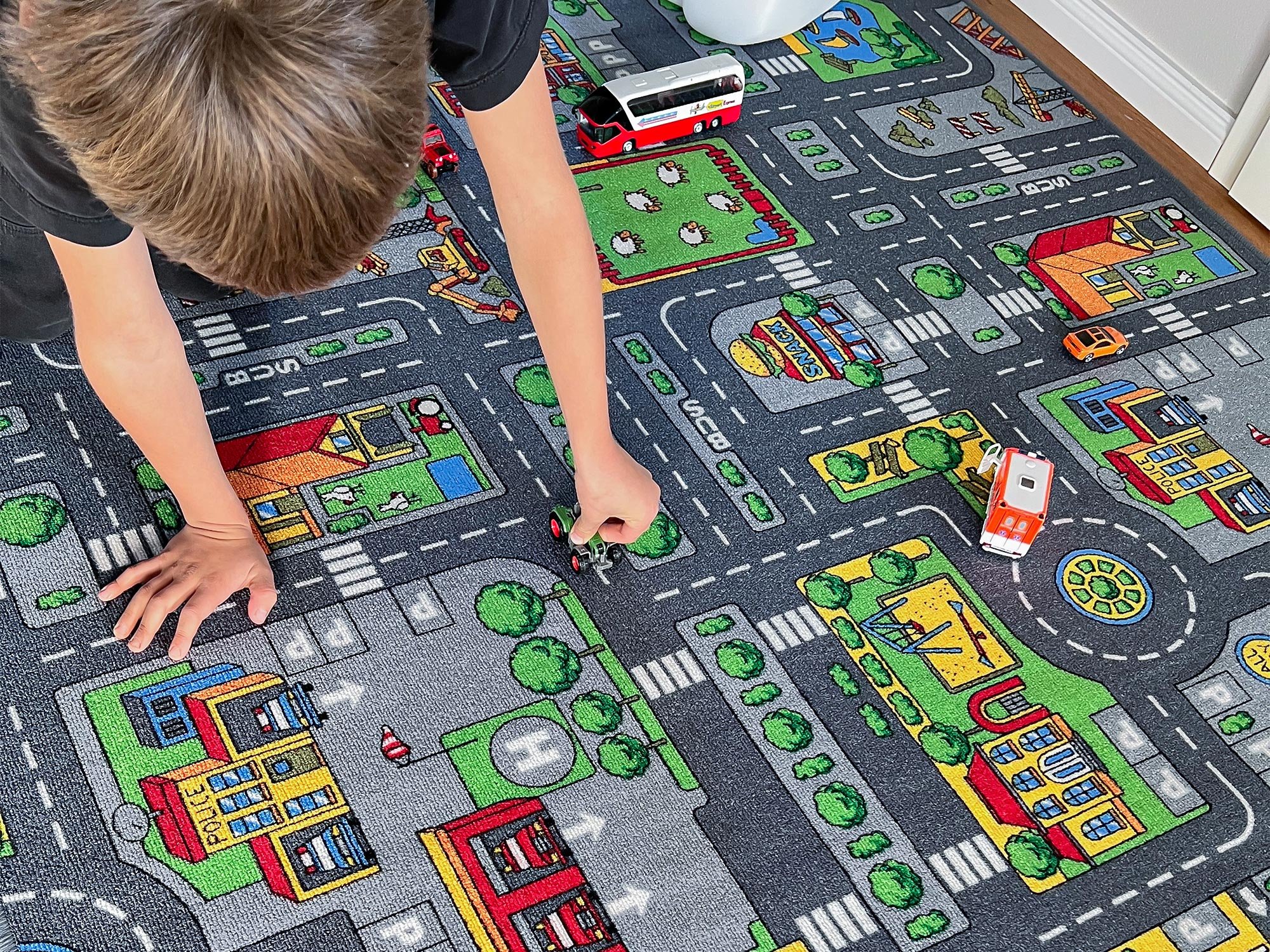 Kind spielt mit kleinen Autos auf buntem Kinderteppich mit Straßenmuster im Kinderzimmer